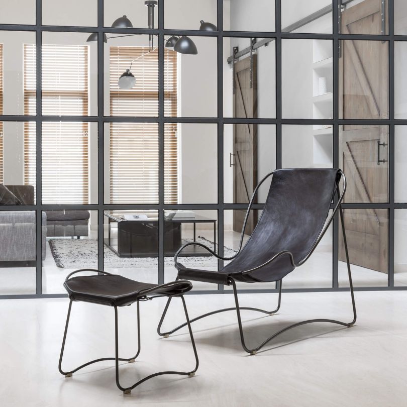 Black leather chaise longue and footstool with metal frame in an industrial interior with steel-framed glass partition