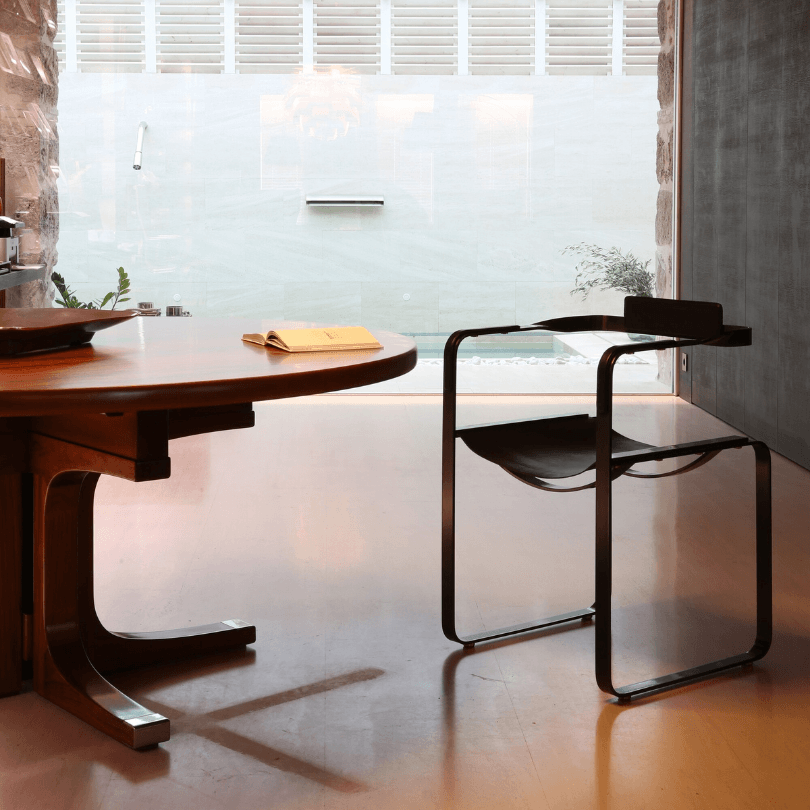 Wanderlust chair in cowhide leather and steel beside a wooden table in an interior overlooking the pool